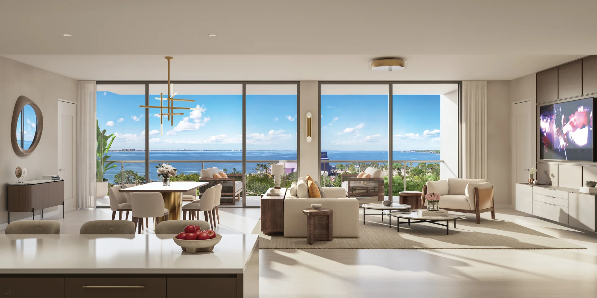 Rendering of a great room seen from a kitchen counter with a bowl of red apples, a dining table with cream chairs under a brass chandelier, a cream sofa and armchairs on a rug, and sliding glass doors to a terrace overlooking the bay.