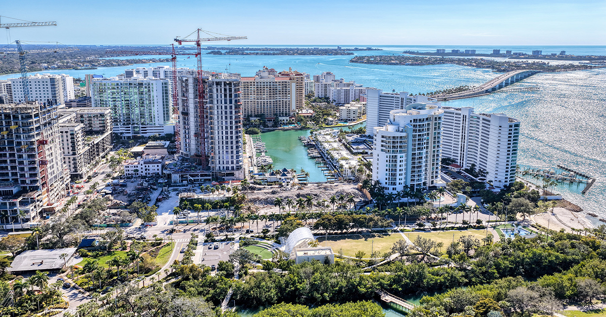 Aerial view of waterfront construction site near marina and bridge over bay.