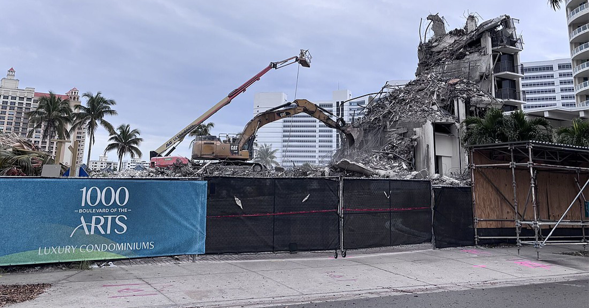 Demolition site with excavators dismantling a concrete building behind fencing