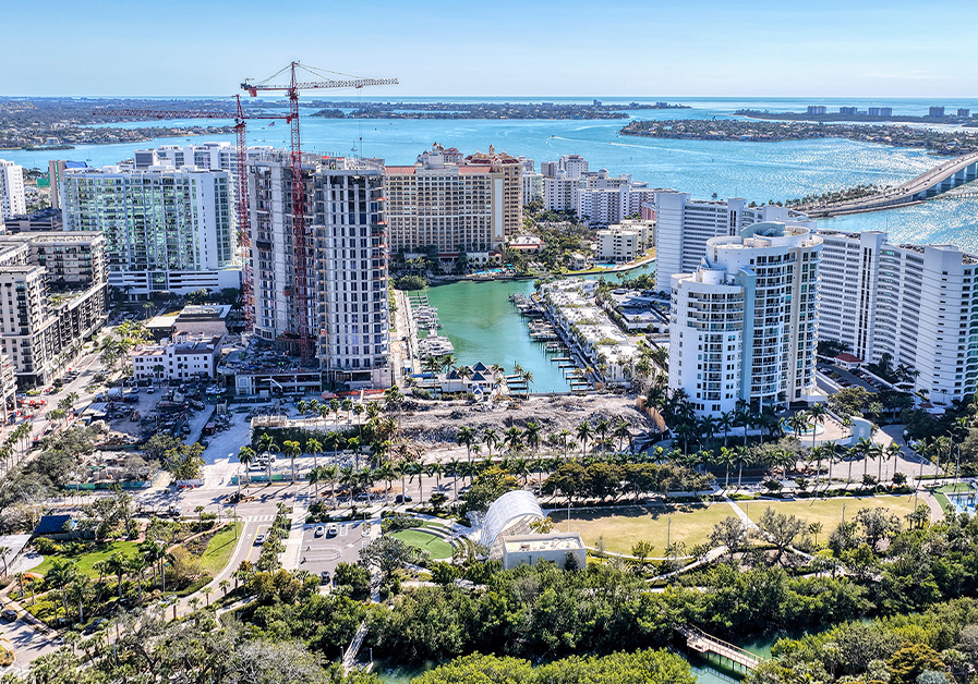 Aerial view of waterfront construction site near marina and bridge over bay.