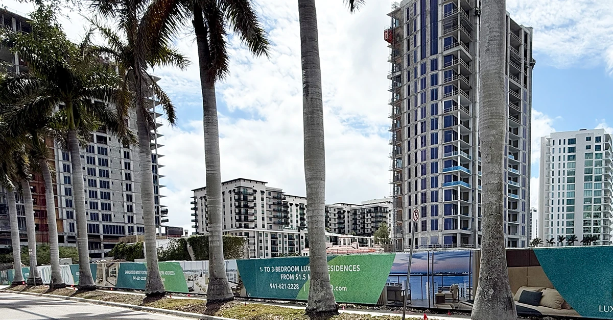 Construction site of high-rise condo with palm trees and nearby buildings